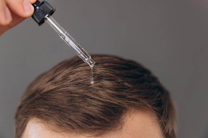 Person applying a dropper of liquid to their hairline